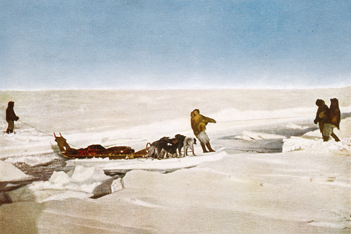 Colored photograph of members of Peary's 1909 expedition crossing an open lead on Arctic sea ice.